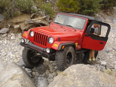1996 Ford Bronco - A person is getting into or out of a red Jeep Wrangler as it drives over a rocky path.