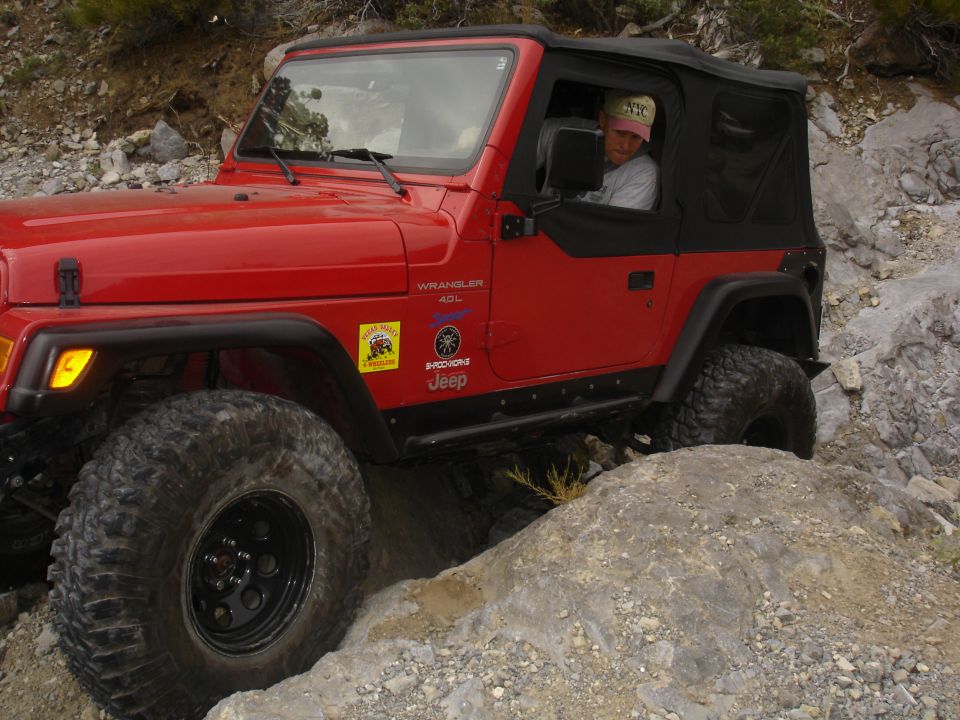 Red Jeep Wrangler 4x4 on rocky terrain, driver wearing a cap