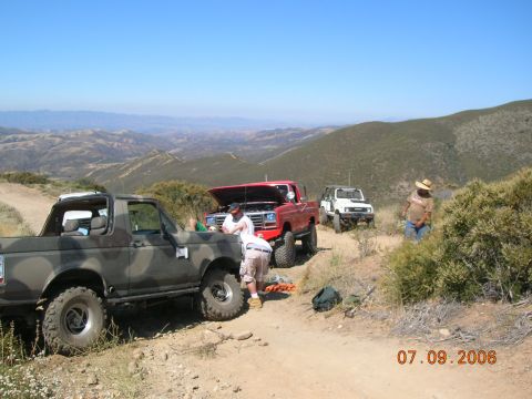 1985 Ford Bronco - A group of off-road vehicles are stopped on a dusty trail with a scenic mountain view in the background.