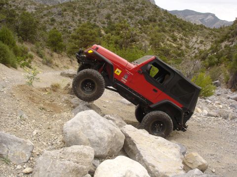 1996 Ford Bronco - A red Jeep Wrangler navigates a rocky off-road trail in a mountainous, arid landscape.