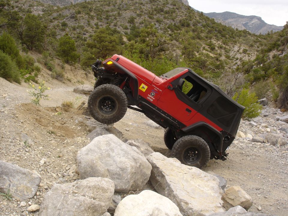 Red Jeep Wrangler climbing over large rocks on a dirt trail