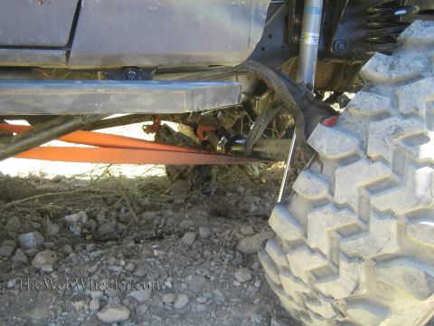 1990 Ford Bronco - Close-up under a lifted off-road truck shows the frame, blue shock, orange tow strap and a chunky mud-terrain tire.