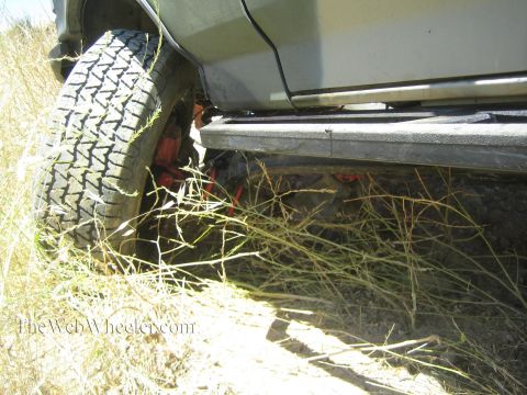 1990 Ford Bronco - truck's mud tire and rocker panel are buried in tall dry brush along a sunlit hillside.
