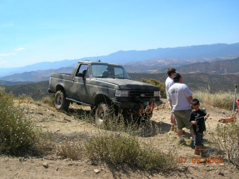 1985 Ford Bronco - A gray Ford Bronco is parked on a dirt road with people standing nearby, overlooking a valley.