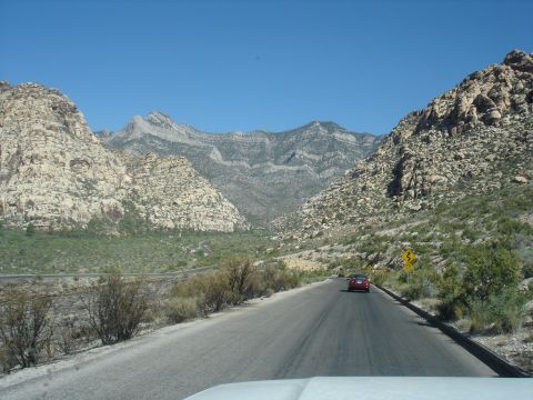 1996 Ford Bronco - A red car travels on a road through a rocky, mountainous area on a clear day.