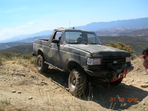 1985 Ford Bronco - A modified Ford Bronco navigates an off-road trail under a clear blue sky.