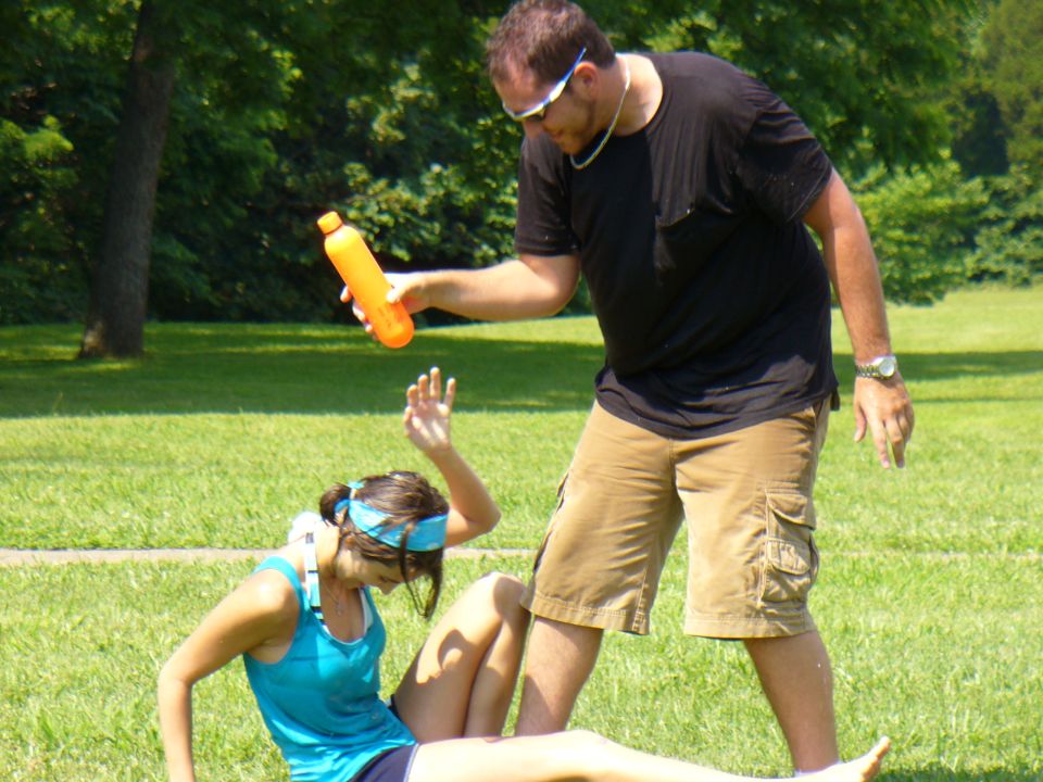 Man holding orange bottle over woman sitting on grass