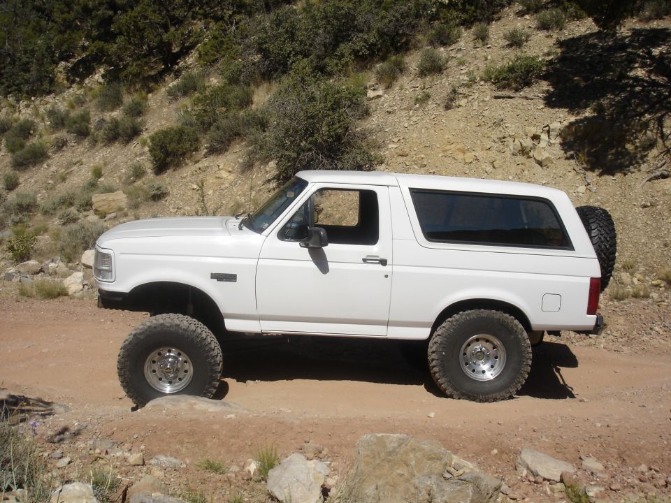 White 1996 Ford Bronco on a dirt road with large tires