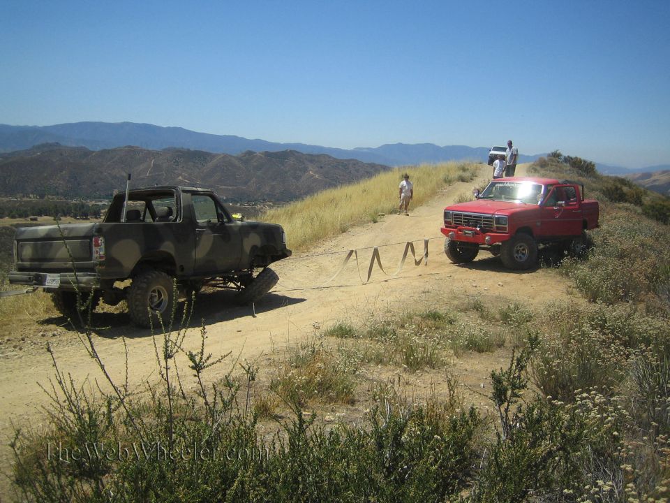 Camo topless Bronco and red lifted truck staged on a hilltop trail
