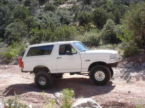 1996 Ford Bronco - A white Ford Bronco is parked on a dirt road in a wooded, hilly area.