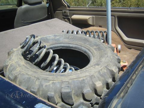 1990 Ford Bronco - large spare off-road tire sits in a vehicle's carpeted cargo area with coil springs stored inside it.