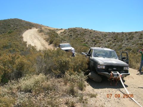 1985 Ford Bronco - A Ford F-Series truck is stuck on a dirt road, with another vehicle visible further up the path.