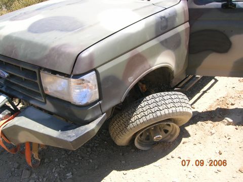 1985 Ford Bronco - Camouflaged Ford truck with a flat tire. The grille suggests a 1987-1991 model year.