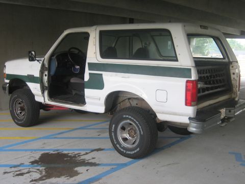 1994 Ford Bronco - This white Ford Bronco with a green stripe is parked in a lot with blue and yellow lines.