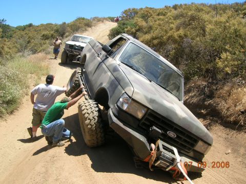 1985 Ford Bronco - Two people push a stuck Ford Bronco on a dirt trail, with another vehicle behind it.