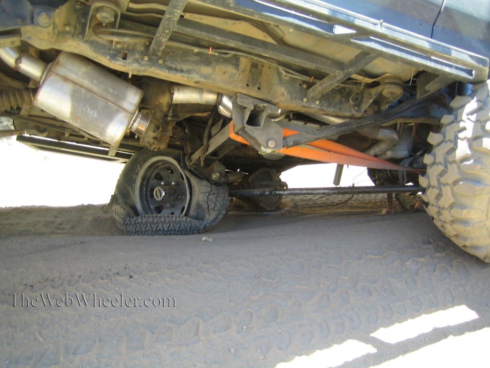 Underbody of a lifted truck showing exhaust, driveshaft and axle on sand