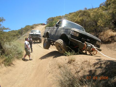 1985 Ford Bronco - Two trucks are on a steep, dusty trail with people nearby.