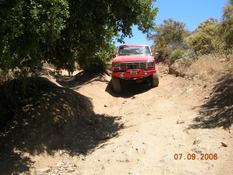 1985 Ford Bronco - Red truck navigates a rough off-road trail on a sunny day.