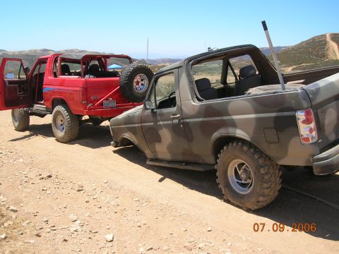 1985 Ford Bronco - Two Ford Broncos are parked on a dusty road under a clear blue sky.