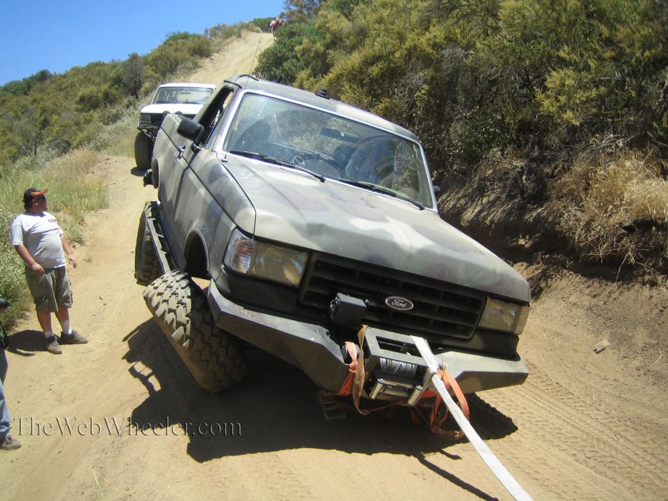 Camo Ford truck tilted on a steep dirt hillside trail with winch line out