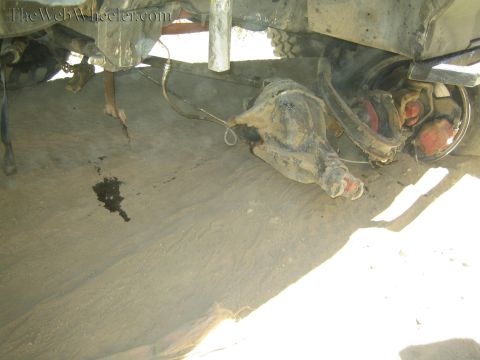 1990 Ford Bronco - Underside of an off-road truck showing a front axle and differential housing dropped down onto the dusty ground.