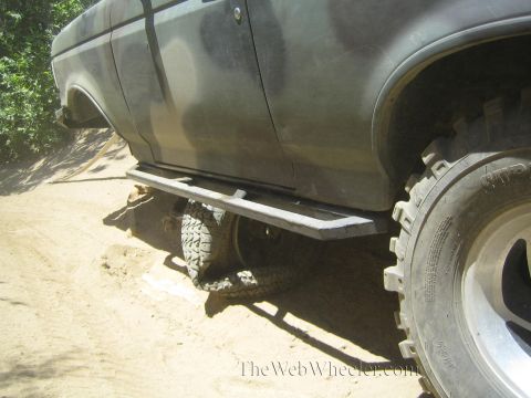 1990 Ford Bronco - Side view of a camo off-road truck's rocker panel and large mud-terrain tire resting on a sandy trail.