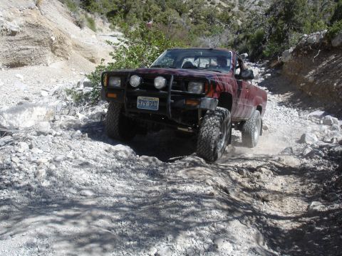 1996 Ford Bronco - A red Toyota pickup truck navigates a challenging rocky terrain on an off-road trail.