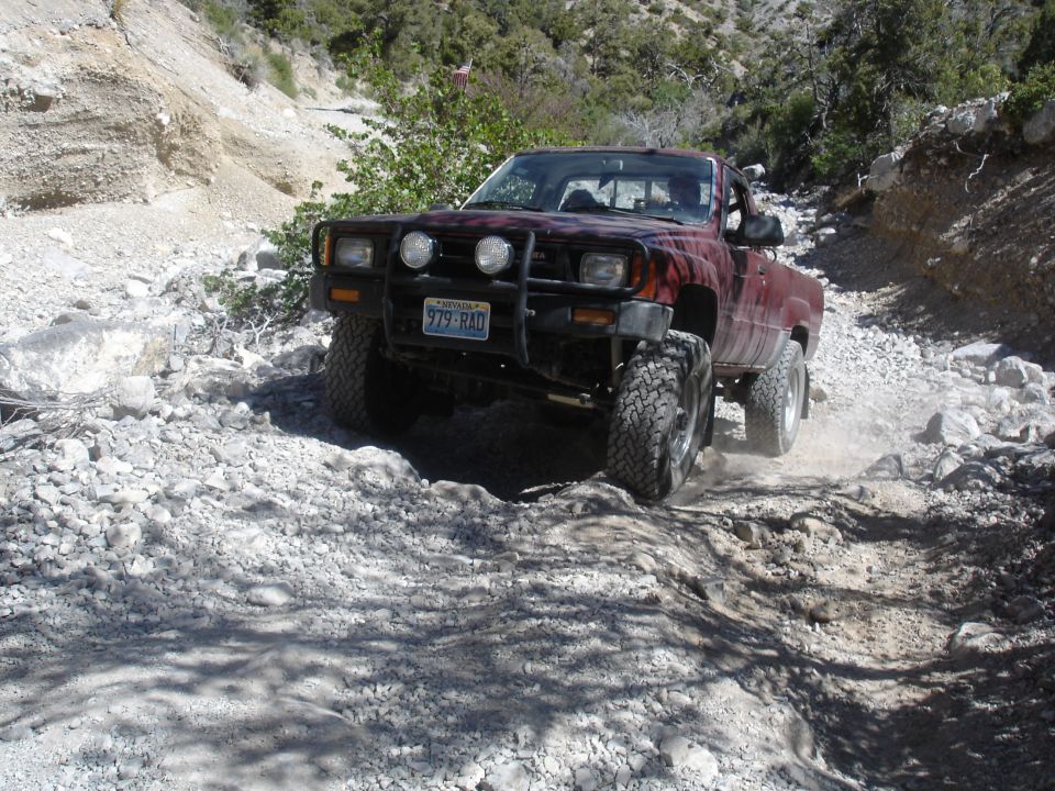 red Toyota pickup truck with bull bar and off-road tires driving on a rocky trail