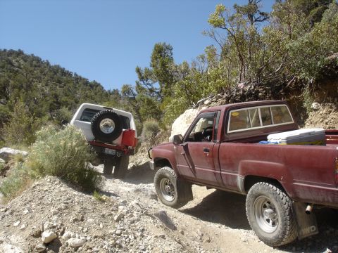 1996 Ford Bronco - Two off-road vehicles navigate a steep, dusty trail under a clear blue sky.