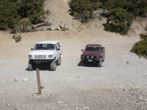 1996 Ford Bronco - Two off-road vehicles, a white Bronco and a maroon pickup, are parked on a gravel road.