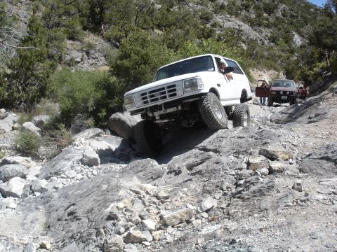 1996 Ford Bronco - White 1996 Ford Bronco tackling a challenging off-road course with other vehicles present.