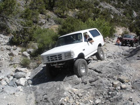 1996 Ford Bronco - A white 1996 Ford Bronco navigates a challenging rocky trail, with another vehicle visible in the background.