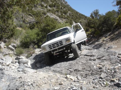 1996 Ford Bronco - White Ford Bronco tackling a challenging rocky off-road path with its door ajar.
