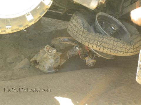 1990 Ford Bronco - Close underbody view of an off-road truck showing the front axle, tire and driveshaft in dusty conditions.