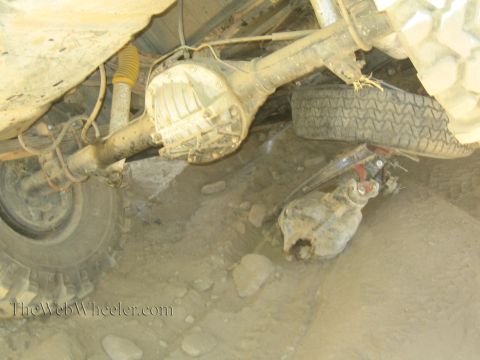 1990 Ford Bronco - Underbody view of an off-road truck showing the rear axle, differential housing, coil spring and suspension over rocky dirt.