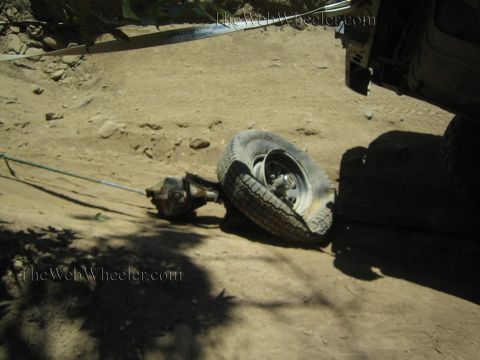 1990 Ford Bronco - detached front axle assembly and wheel lie on the dusty ground beside an off-road truck on a trail.
