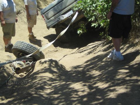 1990 Ford Bronco - Several men stand around a light-colored pickup as a wheel and recovery strap rest on the shaded sandy trail.