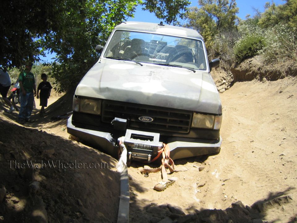 White Ford pickup with front winch on a dirt trail, two people walking past