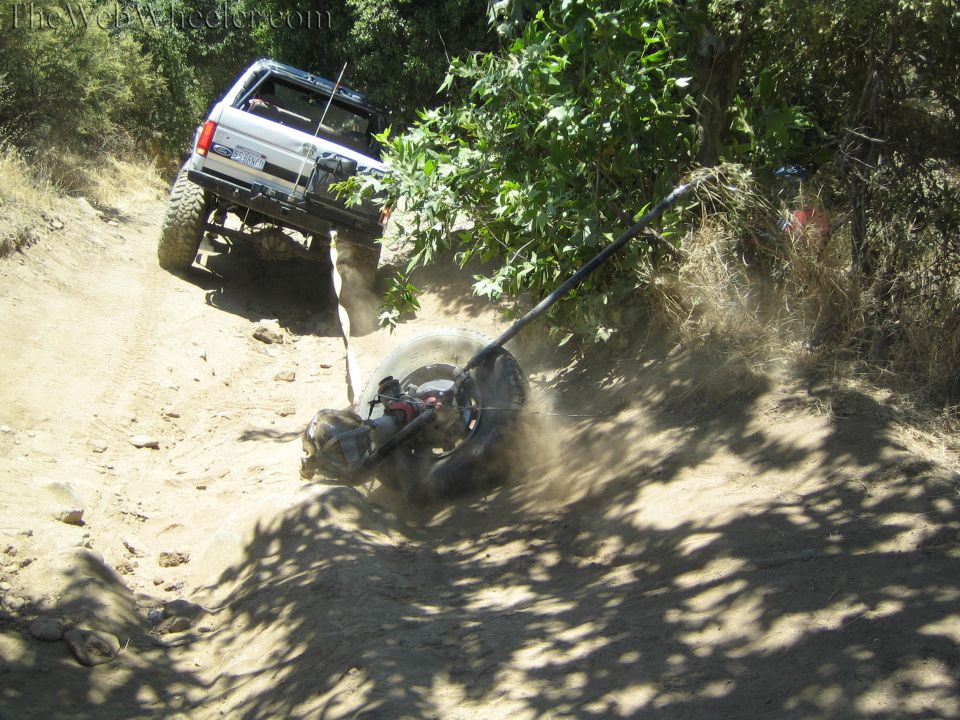 Lifted SUV climbing a dusty hill with a detached axle and tire dragging behind on a strap