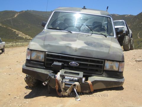 1990 Ford Bronco - camo Ford truck sits front-end-down on a dirt lot, its front axle broken and winch hanging from the bumper.