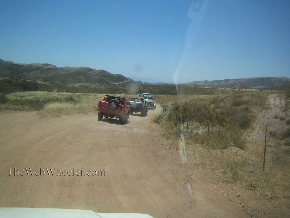 Red and white trucks driving on dirt trail through dry desert hills
