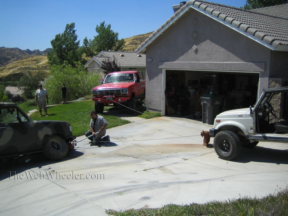 Driveway with camo truck, red Ford pickup, and white Suzuki 4x4 by garage