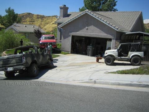 1990 Ford Bronco - camo-painted truck, a red Ford pickup, and a white Suzuki 4x4 sit across a wide concrete driveway in front of a tile-roofed house.