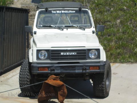 1990 Ford Bronco - Front view of a white Suzuki Samurai 4x4 with a black soft top, off-road tires, and a windshield sticker reading The Web Wheeler.