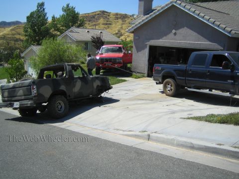 1990 Ford Bronco - camo-painted truck, a red Ford pickup, and a blue Ford crew-cab pickup are parked across a suburban driveway near a garage.