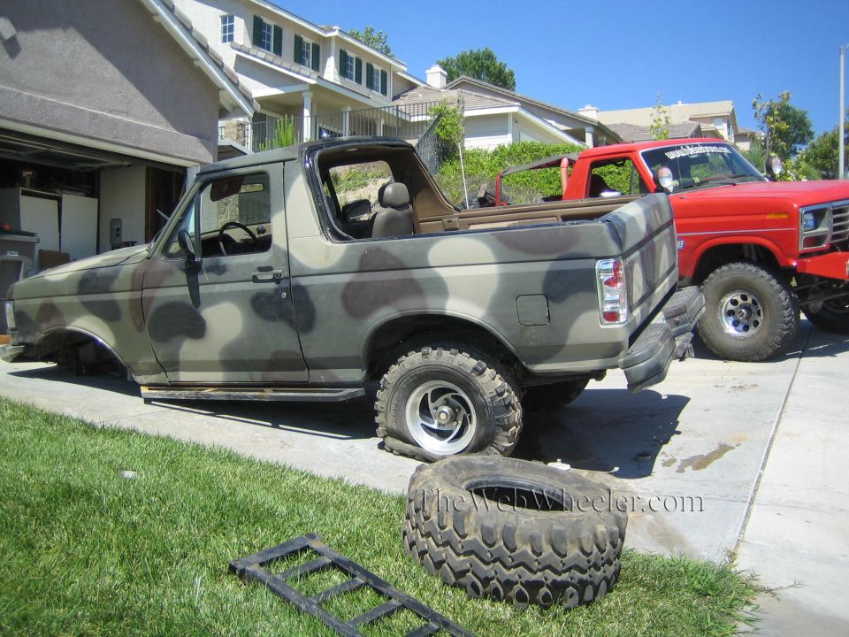Camo Ford SUV with top off beside a red Ford truck, tires on lawn