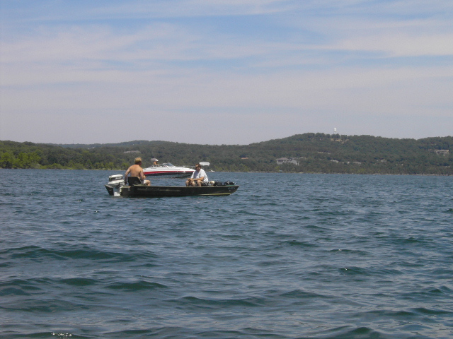Dark green jon boat with outboard motor and two anglers on open lake water