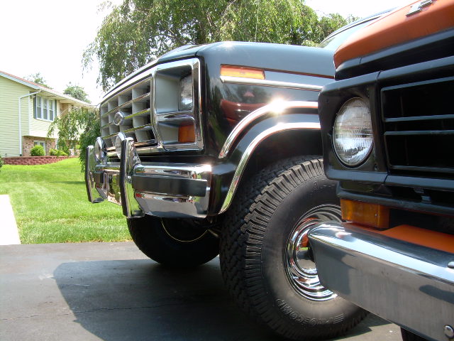 Black 1978 Ford Bronco front corner with chrome grille and bumper, parked next to an orange vehicle