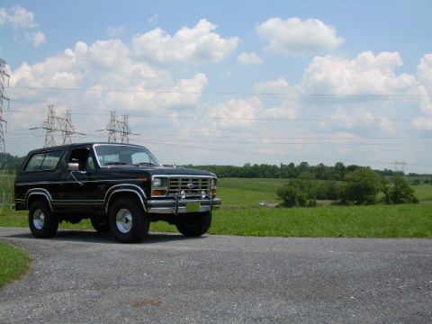 1984 Ford Bronco - Black Ford Bronco parked on a gravel road with a rural landscape and power lines under a cloudy sky.