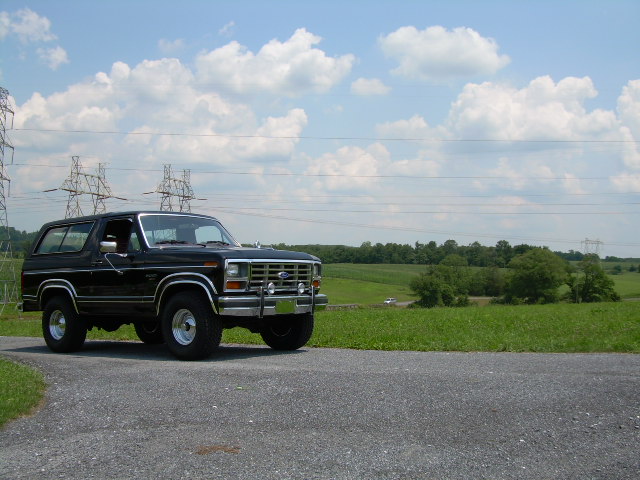 Black 1980s Ford Bronco parked on a gravel road with power lines and fields in the background